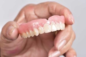 Hand holding dentures noting the difference between complete dentures and partial dentures