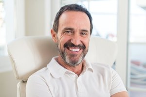 Smiling man in dental chair used to ask what is a dental bridge